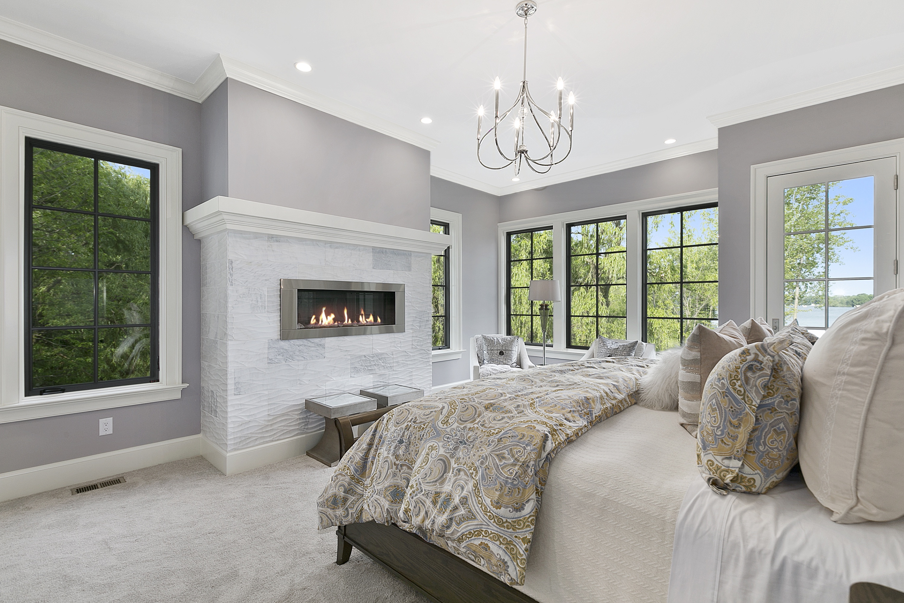 Transitional luxury master bedroom with marble surround linear fireplace and modern chandelier — the rooms that win on Mansion Global