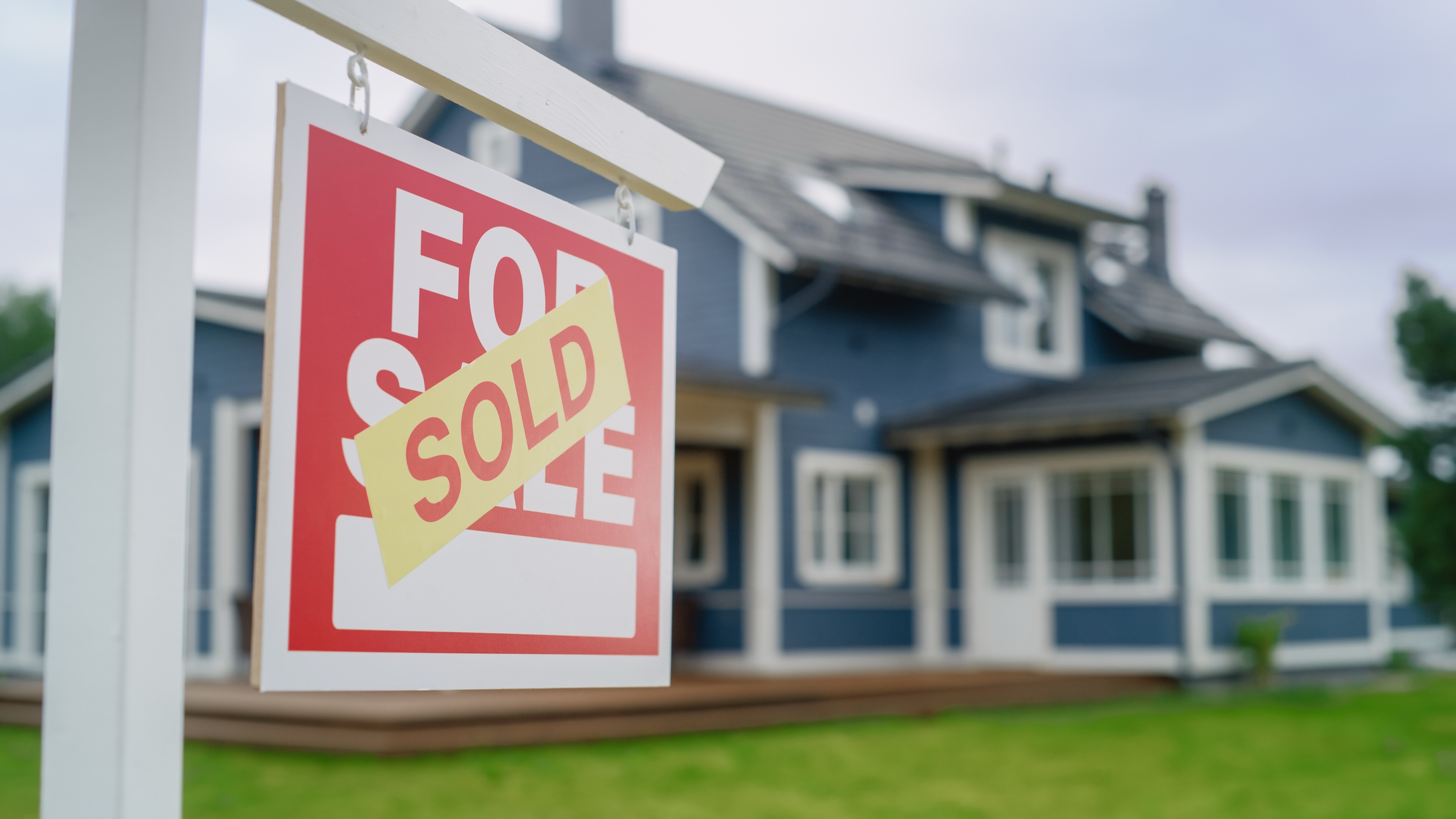 Sold sign on the lawn in front of a large modern house