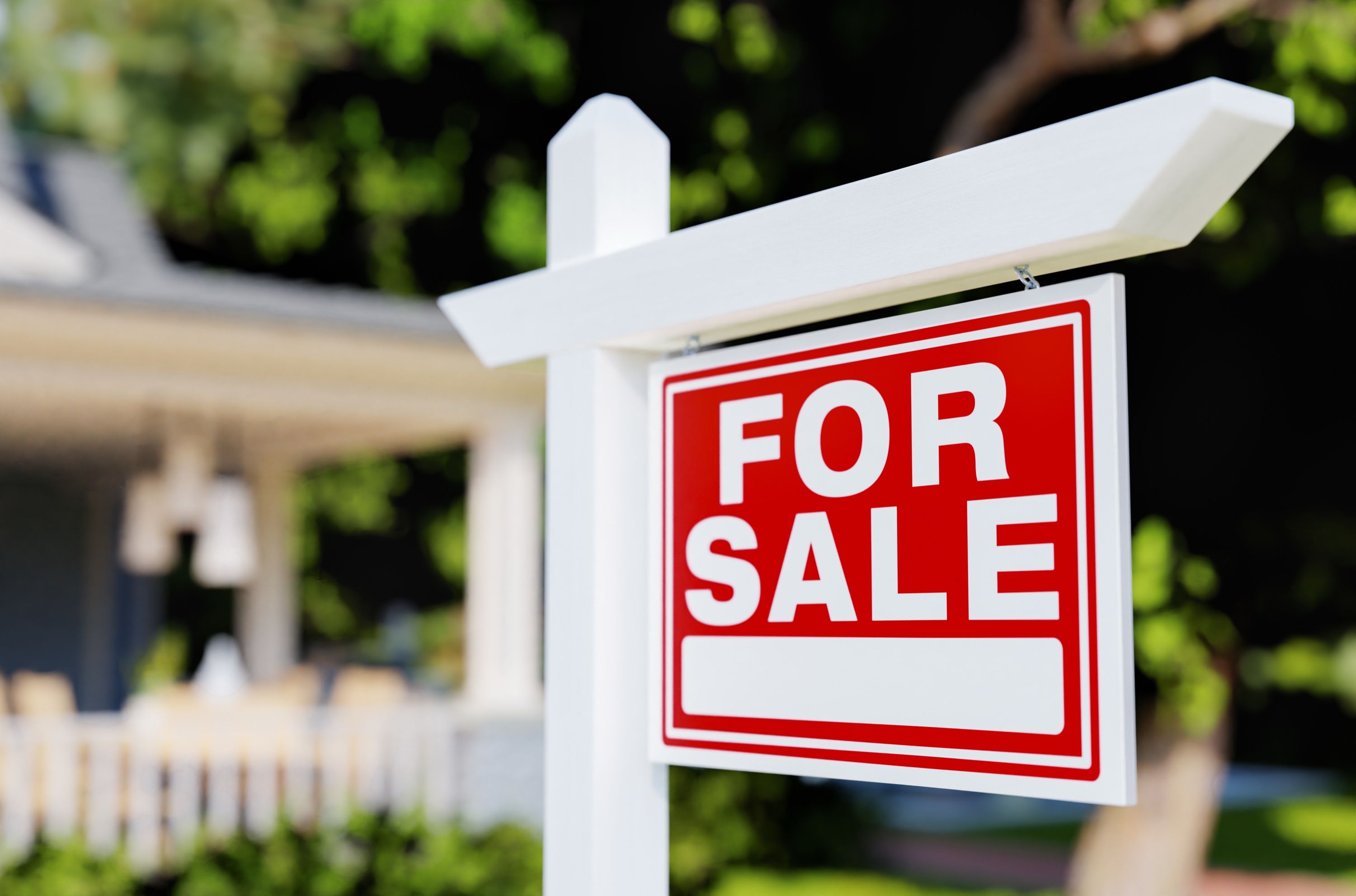 A crisp red For Sale sign on a white post in front of a home