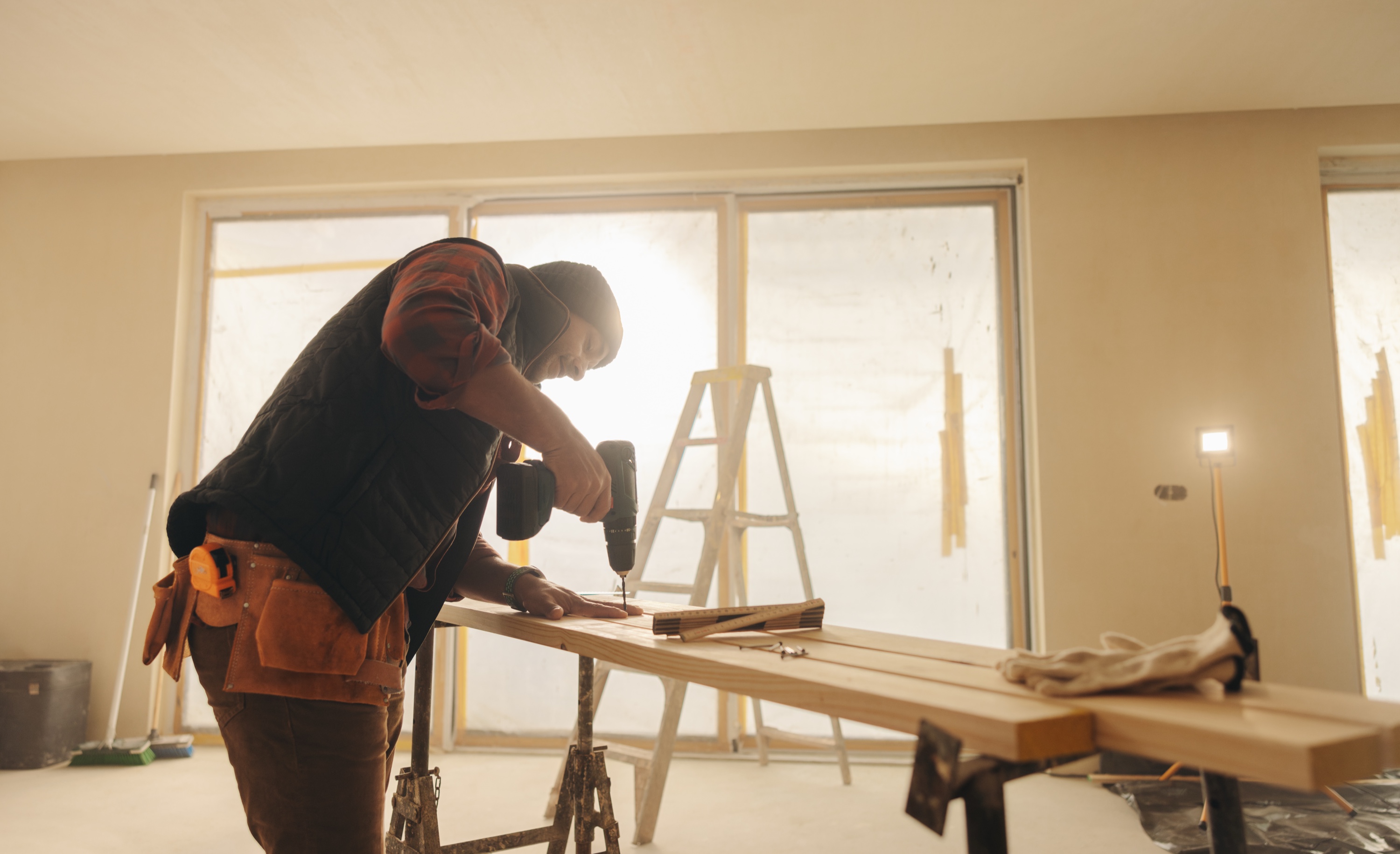 Contractor in tool belt using cordless drill on lumber during a renovation