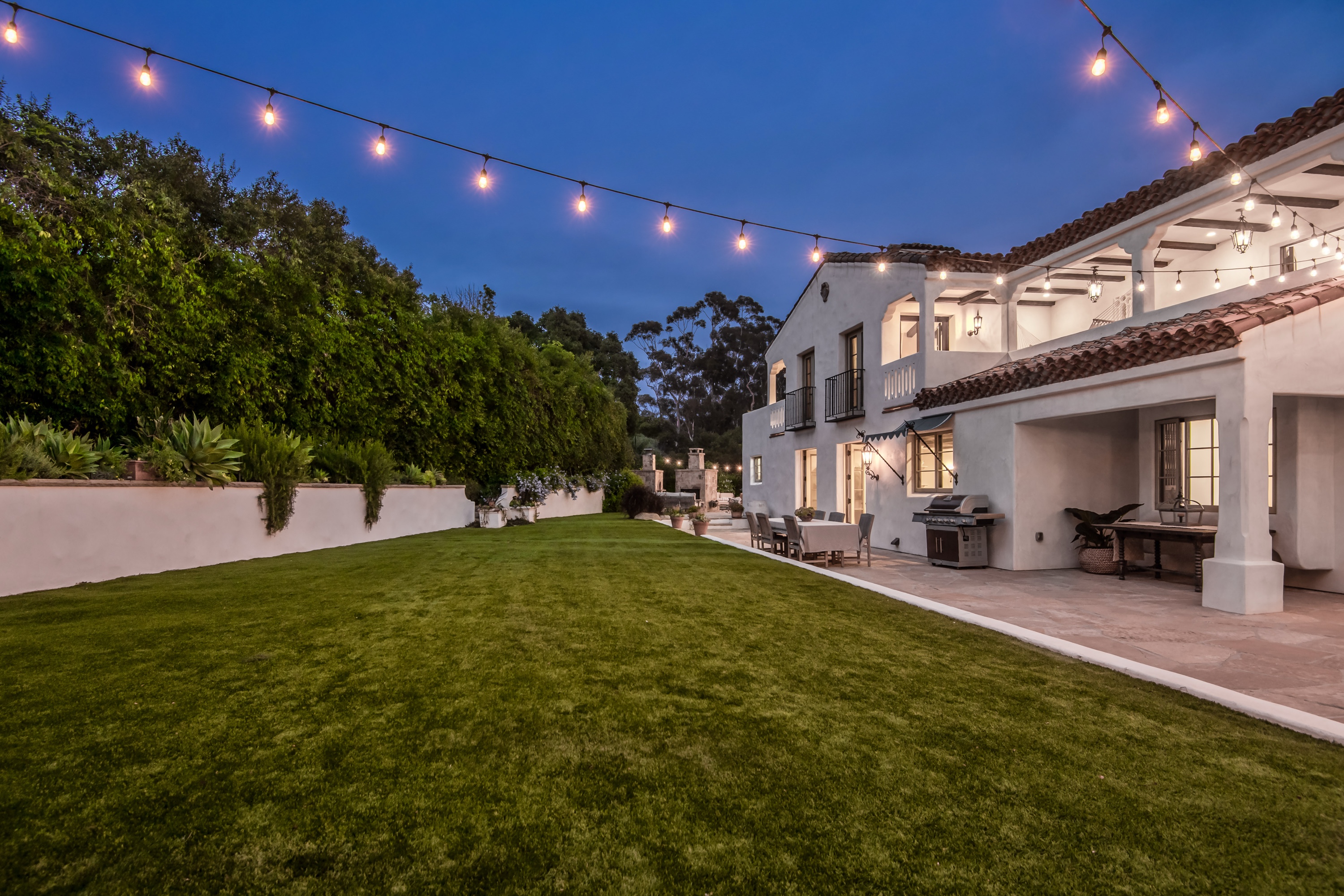 A private outdoor patio with lawn chairs and string lights along a fence at a residential property