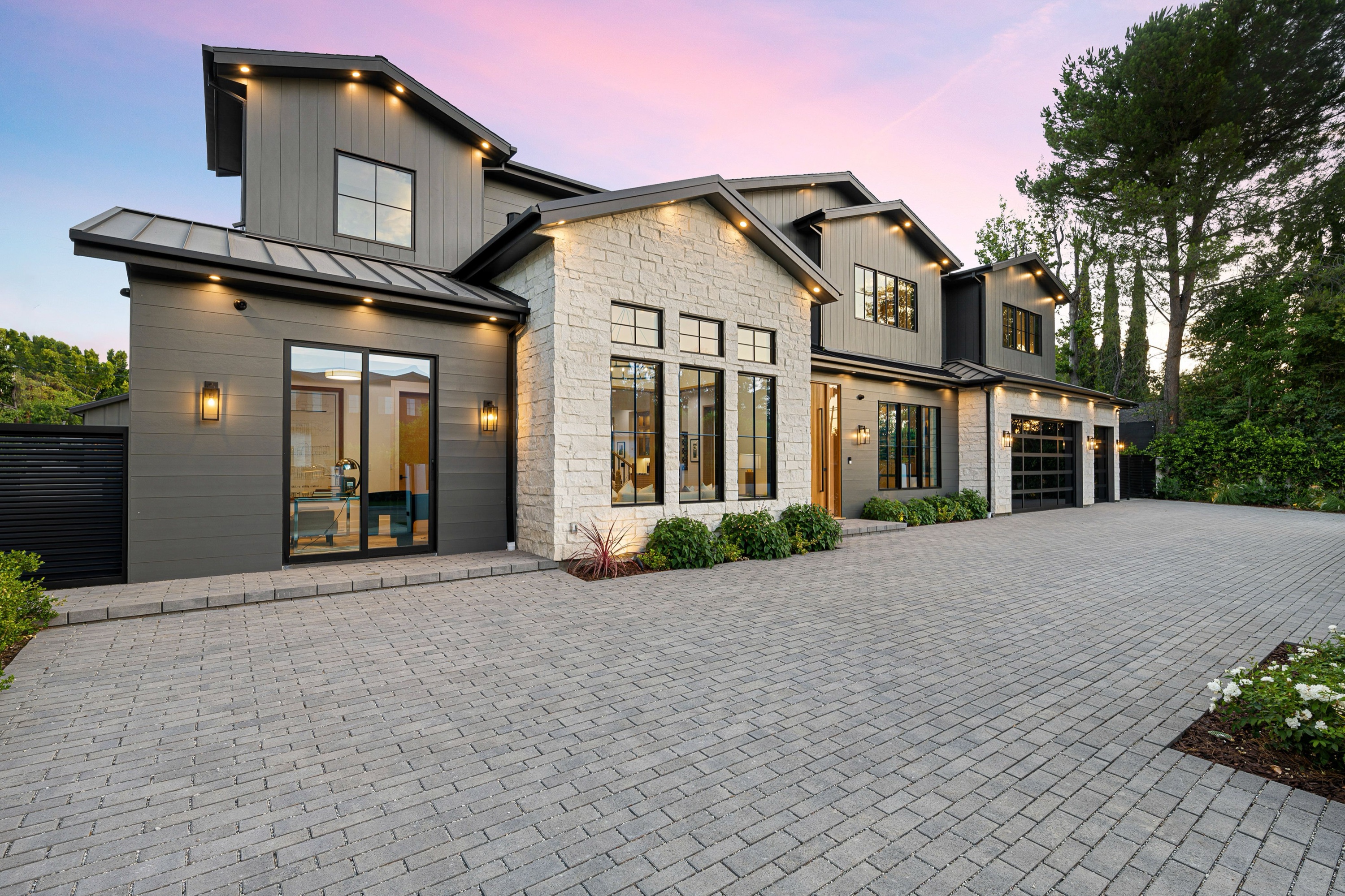 Modern luxury home exterior with large windows and stone detailing at sunset