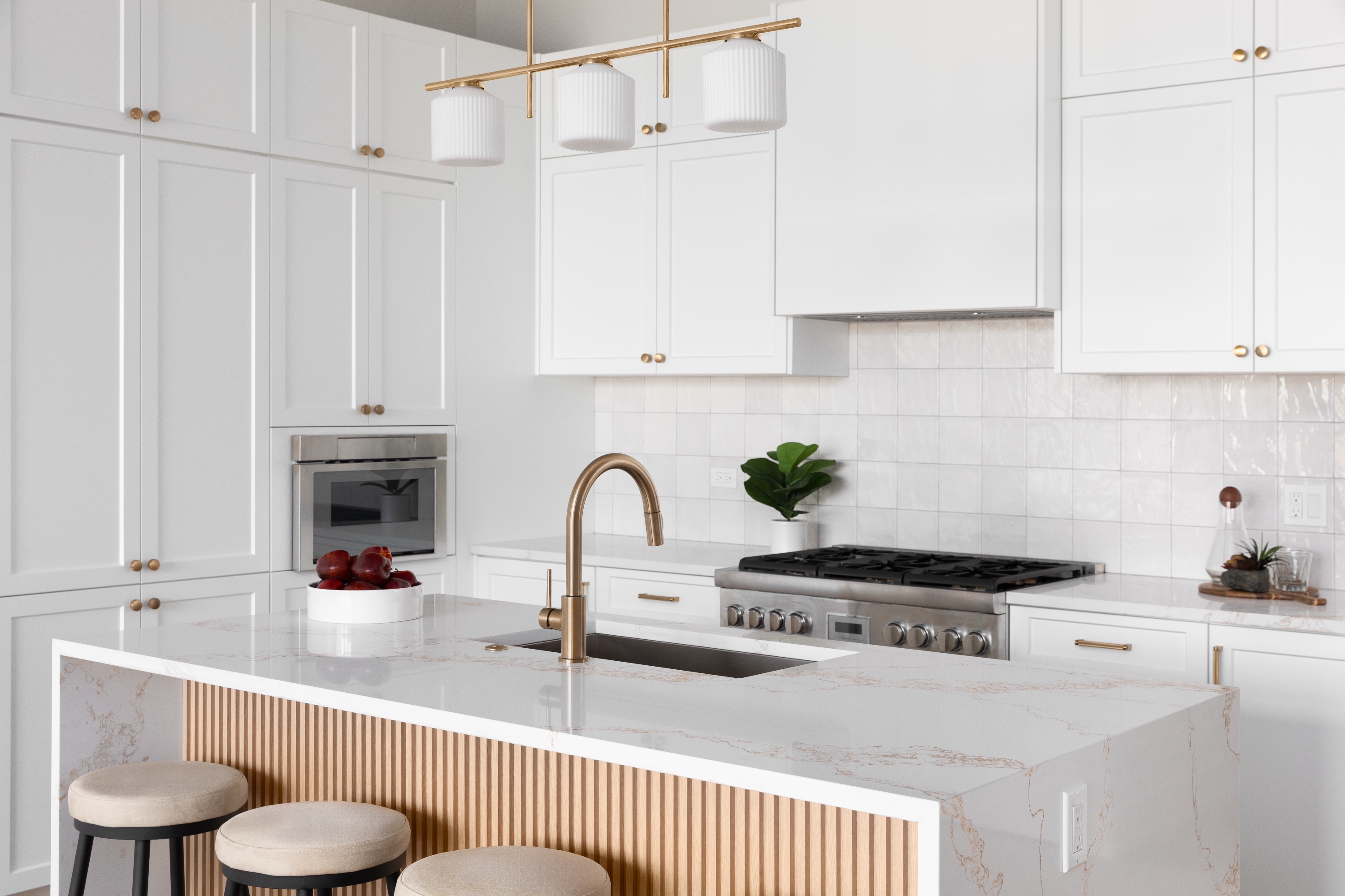 Renovated white kitchen with gold accents and a waterfall marble island