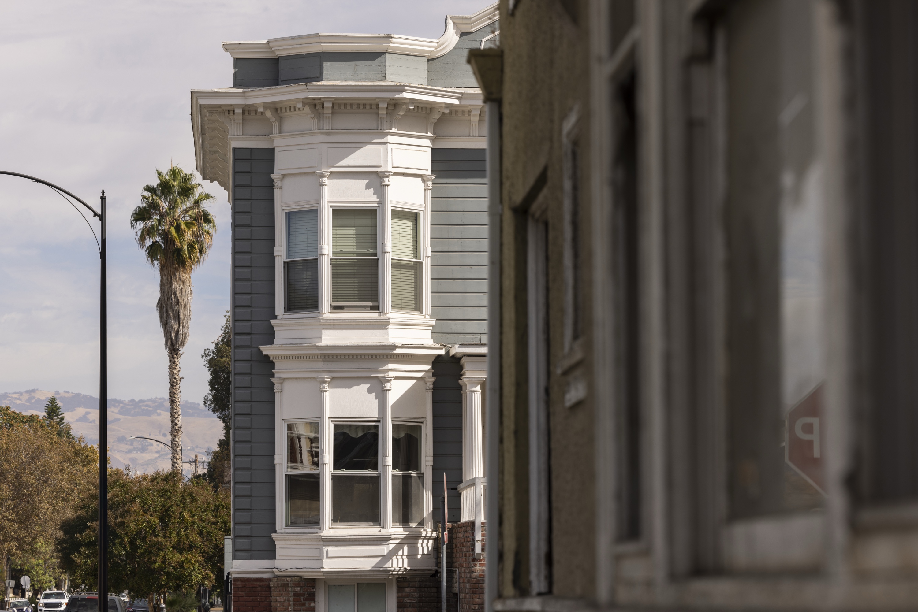 Historic multi-unit Victorian building painted blue and grey with white trim and multiple bay windows, palm tree at the corner